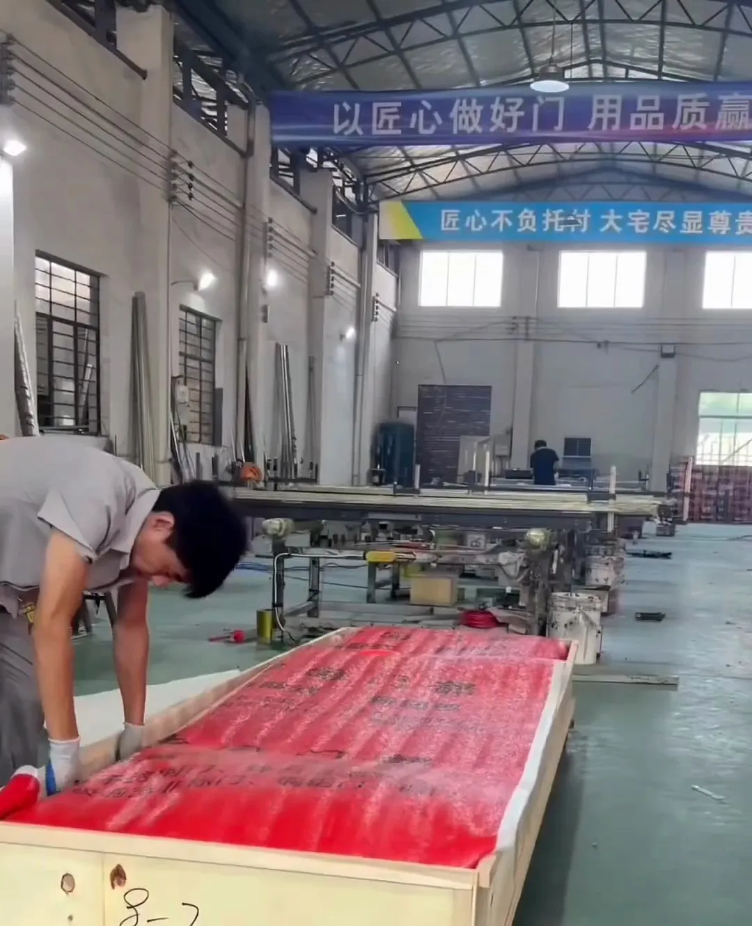 A worker packing a door, covered in a red protective sheet, into a wooden crate