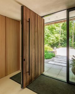 Modern vertical wood slat pivot door with long black bar handle and large glass sidelights for villa entrance