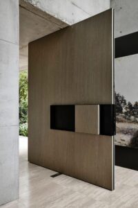 Modern pivot door with light grey concrete texture finish and integrated vertical recessed handle.