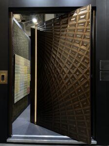 Luxury brushed bronze pivot door with handcrafted 3D geometric pyramid texture and signature warm LED-backlit integrated recessed handle.