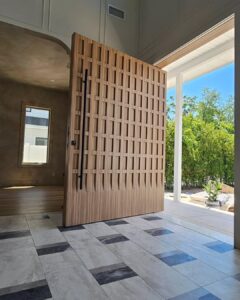 Luxury light wood pivot door with a unique 3D waffle lattice texture and long black bar handle in a bright modern interior.