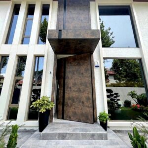 Seamless flush-mount pivot door integrated into matching deep bronze metallic wall cladding with vertical linear grooves.