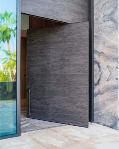A modern Italian-style cast aluminum armored door in slate grey, featuring an asymmetrical gold-tone cross inlay and two vertical recessed flush handles with an integrated smart lock.