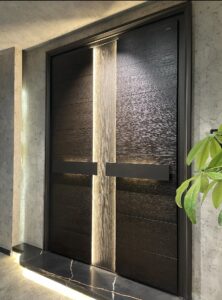 A luxury double armored door with a dark, heavy-textured wood grain, featuring a vertical central LED light strip and two horizontal handles with warm integrated backlighting.