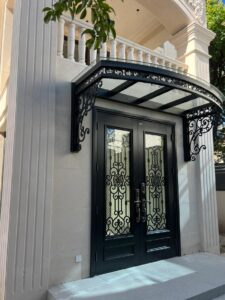 Luxury black French-style double entrance door with intricate wrought-iron scrollwork over glass panels, featuring a matching ornate black iron and glass canopy, set against a neoclassical light stone facade.