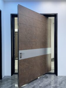 Flush-mount pivot door in aged bronze rust texture with horizontal linear divisions and brushed stainless mid-band featuring lever handle, seamlessly integrated into matching wall cladding.