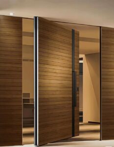 Flush-mount pivot door in natural horizontal wood grain with matte black vertical divider strips and full-height stainless cylindrical pull, seamlessly integrated into matching wood-paneled wall in modern interior.