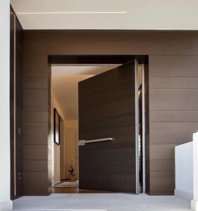 Flush-mount pivot door in deep matte bronze with broad horizontal banding and full-width slim stainless horizontal pull, seamlessly integrated into matching wall cladding with ambient linear LED lighting in luxury interior.