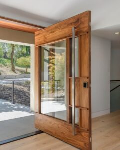 Luxury walnut wood pivot door with a large clear glass inlay and an oversized vertical stainless steel bar handle.