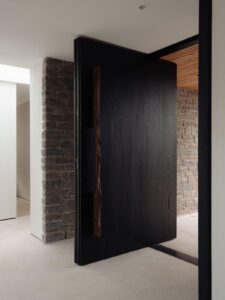 Bespoke luxury black charcoal pivot door with organic full-height live-edge wood vertical bar handle and integrated security.