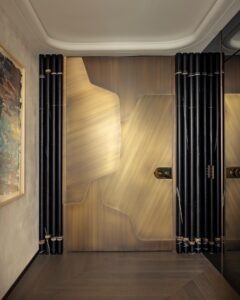 Luxury Art Deco pivot door in brushed champagne gold with asymmetrical geometric patterns and a large circular mechanical handle.