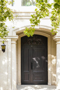 Luxury French-style double entrance door in antique bronze cast aluminum, featuring ornate royal relief carvings, an arched stone frame, and a modern black smart handle.