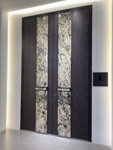A symmetric double armored door with a dark, textured point-patterned surface and two large vertical natural stone inlays featuring complex white, gold, and black veining. Includes recessed rectangular handles and a smart lock.